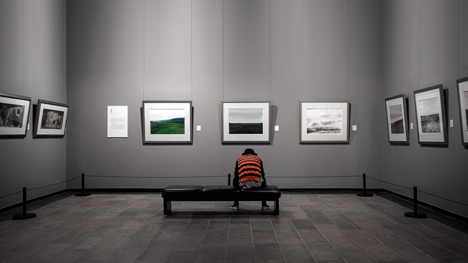 Galerie d'art presque vide, un visiteur seul assis face aux cadres